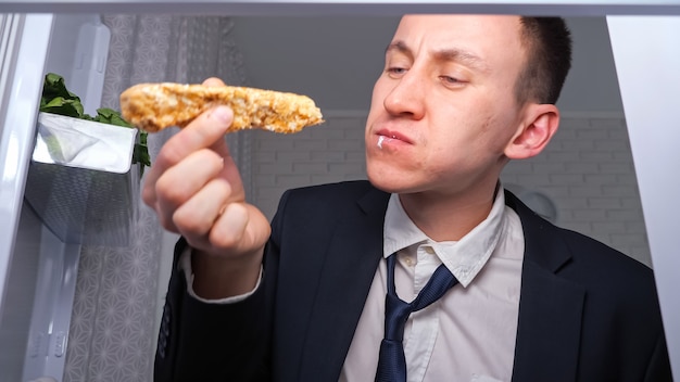 Foto hombre de negocios hambriento come pepino con tortas en la cocina oscura