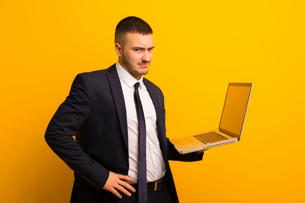 Hombre de negocios hermoso joven contra el fondo plano que sostiene una computadora portátil