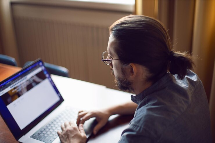 Foto hombre de negocios un hombre con barba y gafas está sentado en una computadora portátil en una mesa de madera en casa