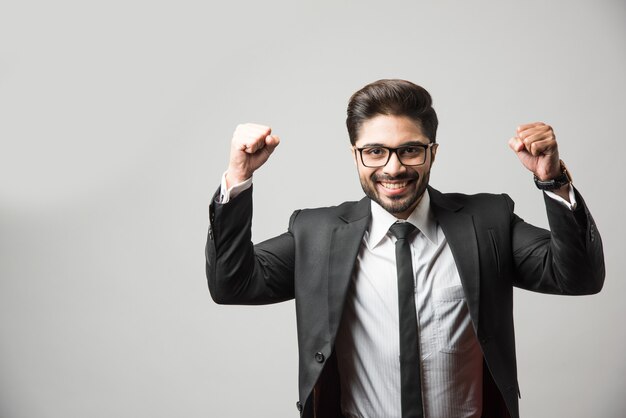 Foto hombre de negocios indio barbudo celebrando el éxito con los pulgares hacia arriba o levantando el puño mientras está de pie aislado sobre fondo negro