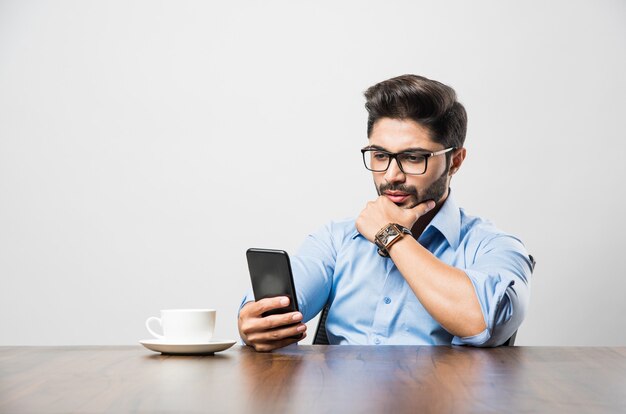 Hombre de negocios indio con teléfono celular. Tener una conversación o escribir o revisar los feeds de las redes sociales