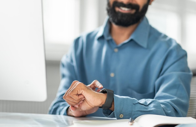 Un hombre de negocios indio tocando un reloj inteligente y mirándolo comprobando la hora usando un dispositivo moderno en