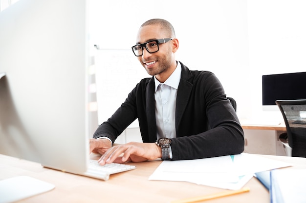 Hombre de negocios inteligente sonriente que trabaja con la computadora en la oficina