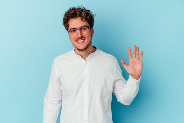 Hombre de negocios joven aislado en la pared azul sonriendo alegre mostrando el número cinco con los dedos