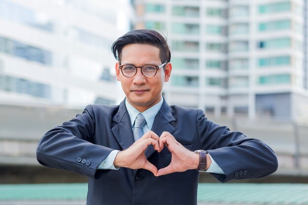 Hombre de negocios joven de Asia que hace un corazón con sus manos sobre el fondo blanco, amo busines