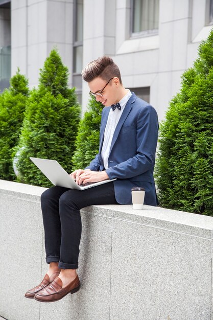 Hombre de negocios joven atractivo con la computadora portátil y el café en las manos en el fondo del edificio de oficinas. trabajando con laptop y smilling.