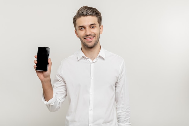 Hombre de negocios joven en camisa blanca con smartphone de pantalla en blanco aislado sobre fondo blanco.