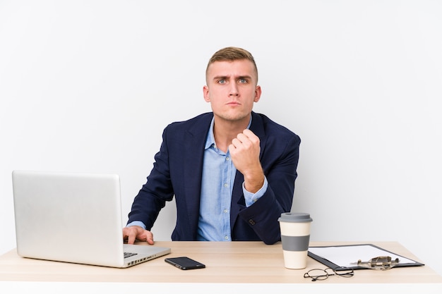 Hombre de negocios joven con una computadora portátil que muestra el puño con la expresión facial agresiva.