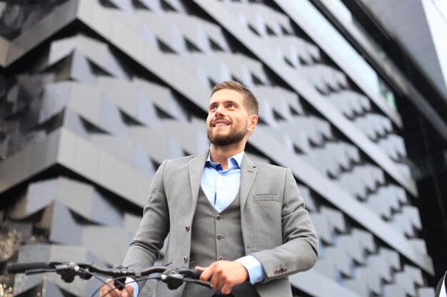 Hombre de negocios joven confidente que camina con la bicicleta en la calle de la ciudad.