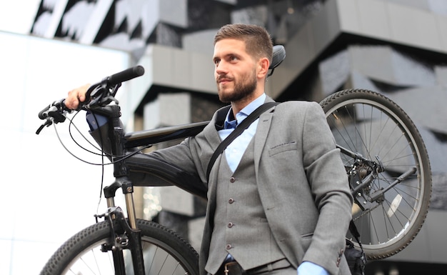 Hombre de negocios joven confidente que lleva su bicicleta mientras camina al aire libre.