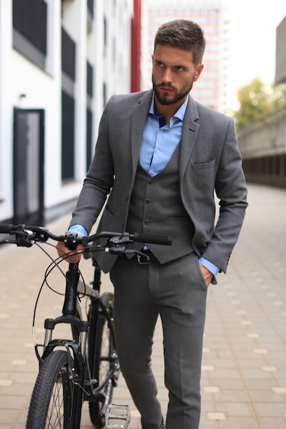 Hombre de negocios joven confidente que lleva su bicicleta mientras camina al aire libre.