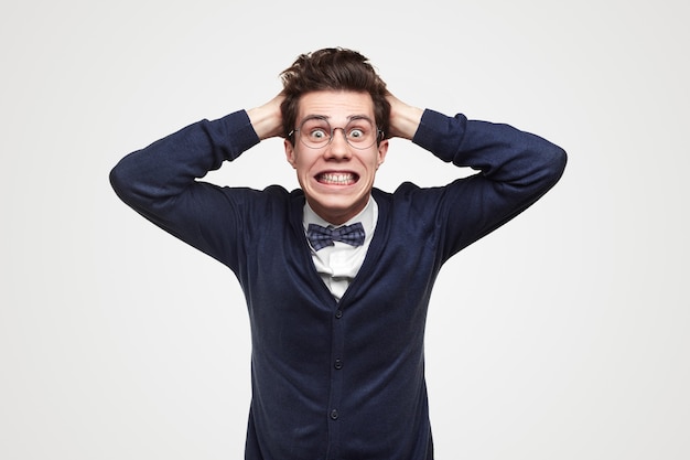 Hombre de negocios joven desesperado con traje elegante y gafas sorprendiéndose con noticias sobre crisis financiera y haciendo muecas