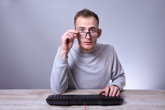 Hombre de negocios joven divertido del empollón, hombre que trabaja en la computadora. Escribiendo en el programador del teclado en vidrios delante de la computadora.