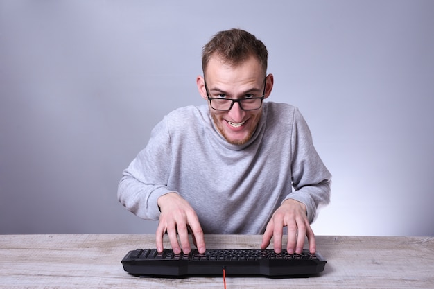 Hombre de negocios joven divertido del empollón, hombre que trabaja en la computadora. Escribiendo en el programador del teclado en vidrios delante de la computadora.