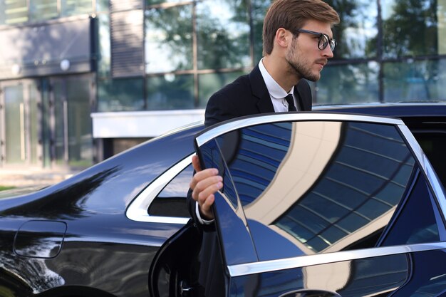 Hombre de negocios joven elegante que entra en su coche mientras está parado al aire libre.