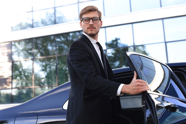 Hombre de negocios joven elegante que entra en su coche mientras está parado al aire libre.