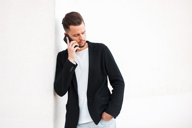 Hombre de negocios joven guapo hablando por teléfono cerca de la pared blanca