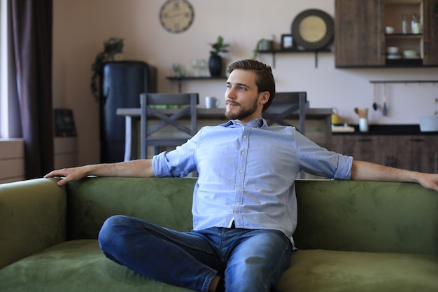 Foto hombre de negocios joven guapo parece relajado mientras está sentado en el sofá en casa.