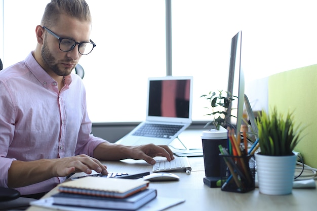 Hombre de negocios joven pensativo en camisa trabajando usando la computadora mientras está sentado en la oficina.