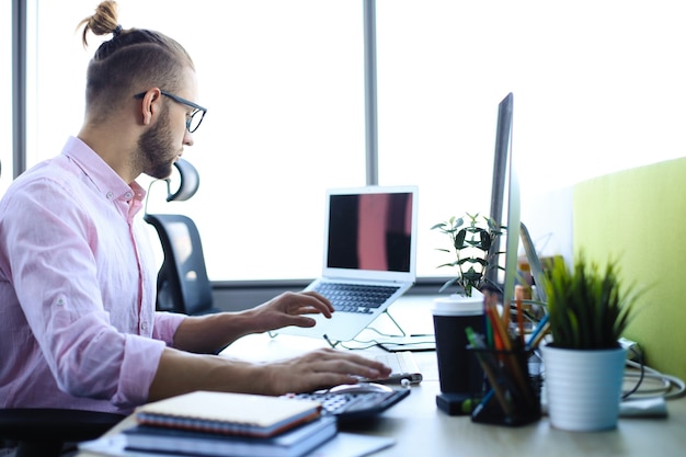 Hombre de negocios joven pensativo en camisa trabajando usando la computadora mientras está sentado en la oficina.