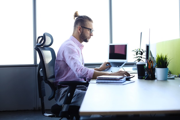 Hombre de negocios joven pensativo en camisa trabajando usando la computadora mientras está sentado en la oficina.