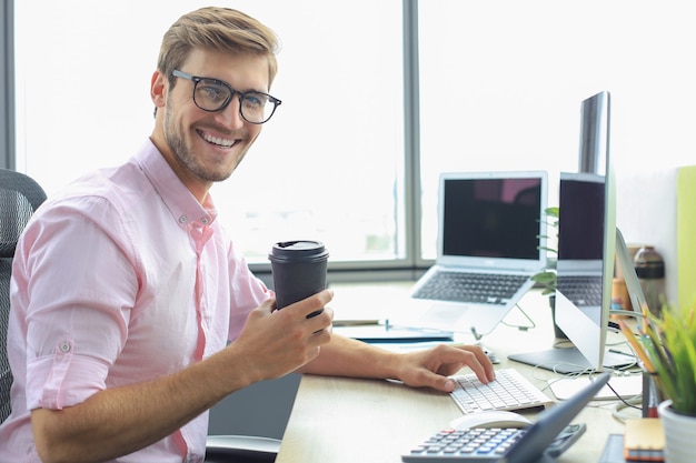 Hombre de negocios joven pensativo en camisa trabajando usando la computadora mientras está sentado en la oficina.