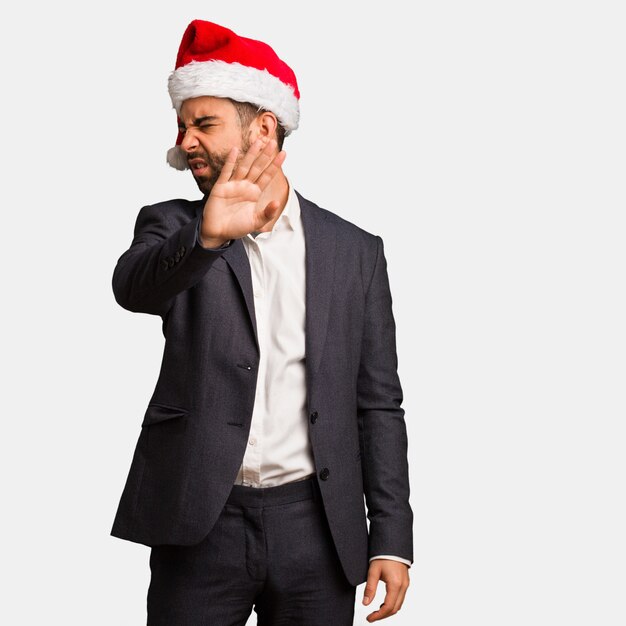 Hombre de negocios joven que lleva el sombrero de santa que pone la mano en frente