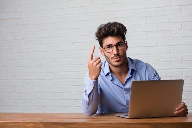 Hombre de negocios joven que se sienta y que trabaja en una computadora portátil que muestra el número uno, símbolo de contar