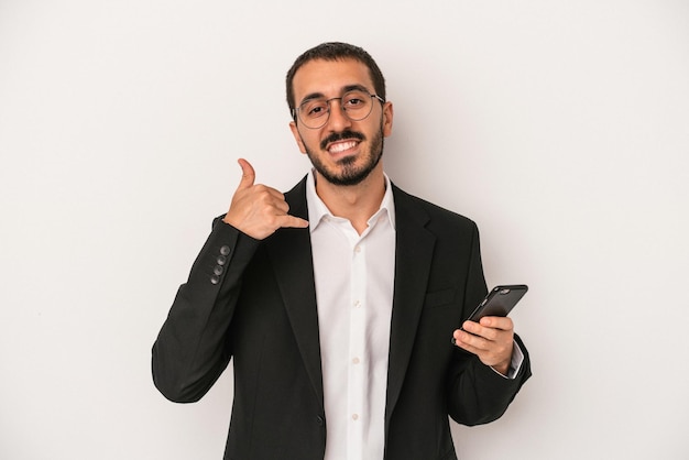 Hombre de negocios joven que sostiene un teléfono móvil aislado en el fondo blanco que muestra un gesto de llamada de teléfono móvil con los dedos