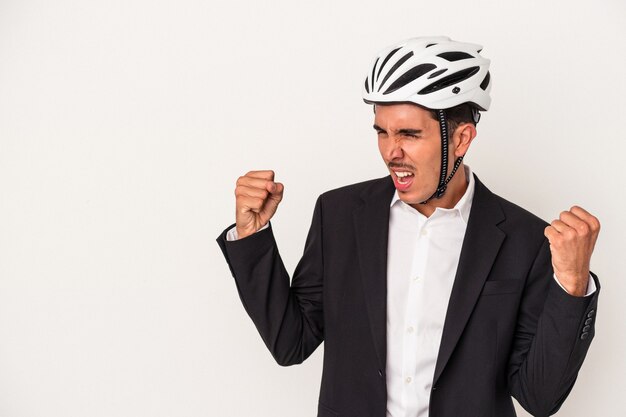 Hombre de negocios joven de raza mixta con un casco de bicicleta aislado sobre fondo blanco levantando el puño después de una victoria, concepto ganador.