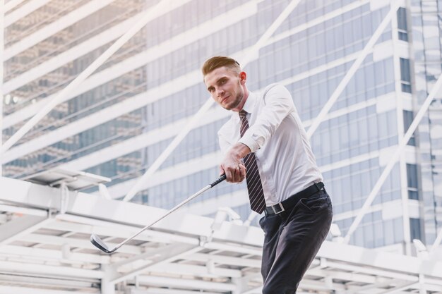 Foto hombre de negocios jugando al golf de pie en el fondo de la ciudad