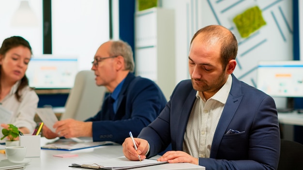 Hombre de negocios leyendo un documento en papel, discutiendo el contrato con un socio seguro, firmando documentos de inversión. Director ejecutivo reuniendo accionistas en oficina de puesta en marcha, con acuerdo satisfactorio.