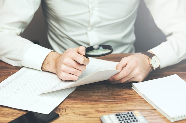 Hombre de negocios leyendo documentos con lupa