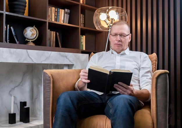 Hombre de negocios leyendo un libro en la biblioteca de negocios sentado en un sillón