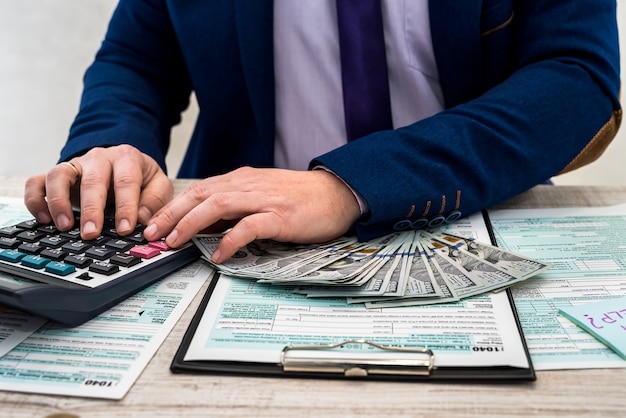 Un hombre de negocios llena un formulario de impuestos individual 1040 y cuenta dólares. Manos masculinas escribiendo en papel con calculadora en la oficina. Concepto de contabilidad