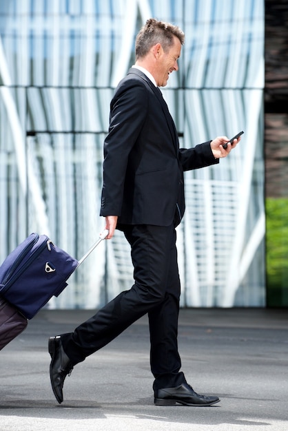 Hombre de negocios de longitud completa caminando con maleta y teléfono móvil
