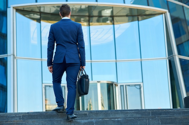 Hombre de negocios con maletín subiendo las escaleras para trabajar, mirar desde atrás