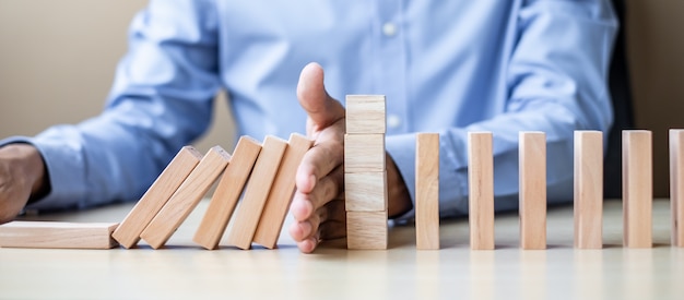 Hombre de negocios mano parando caer bloques de madera o dominó