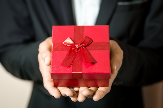 Hombre de negocios mantenga la caja de regalo roja en las manos.