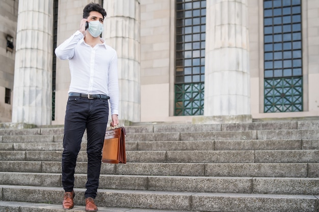 Hombre de negocios con una mascarilla mientras habla por teléfono al aire libre