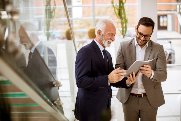 Hombre de negocios mayor que señala y que muestra algo al socio menor en la tableta digital en la oficina