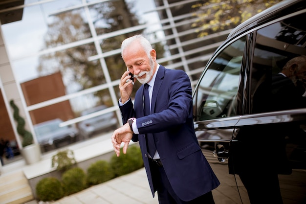 Hombre de negocios mayor que usa el teléfono móvil cerca del coche