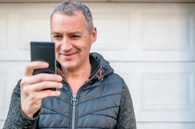 Foto un hombre de negocios de mediana edad caminando al lado del edificio de oficinas mientras utiliza su teléfono inteligente