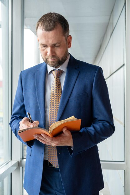 Un hombre de negocios de mediana edad enfocado en un traje escribe notas en un diario personal planea un día de trabajo revisa un horario