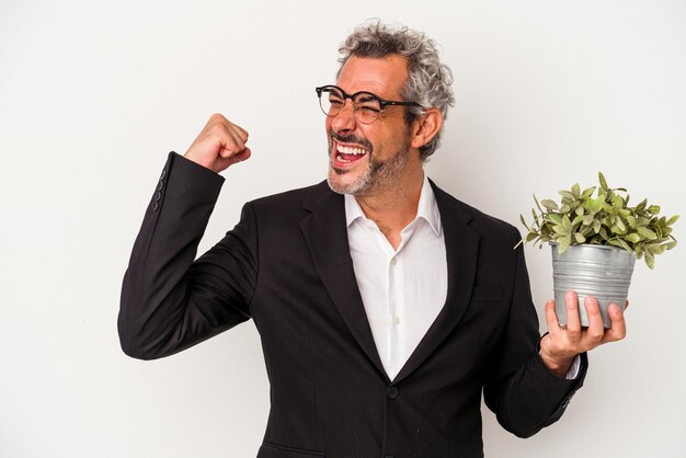 Foto hombre de negocios de mediana edad sosteniendo una planta aislada en fondo blanco levantando el puño después de una victoria, concepto ganador.