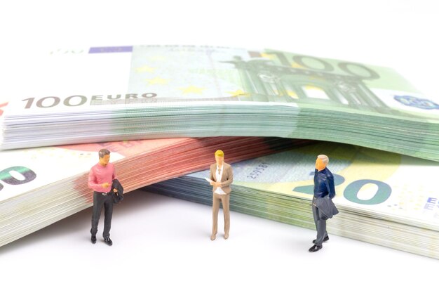 Un hombre de negocios en miniatura navega por el paisaje financiero rodeado de billetes de euro.