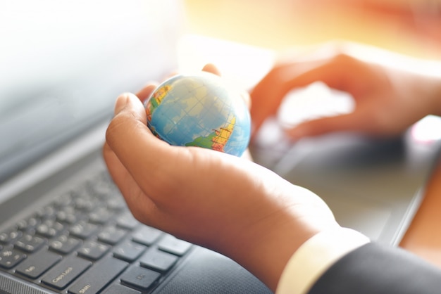 Hombre de negocios con el modelo de globo terráqueo en la mano y usar una computadora portátil - Concepto de tecnología empresarial global y mundial