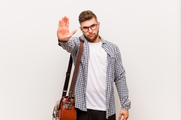 Hombre de negocios moderno joven de pie con la mano extendida que muestra la señal de stop, impidiéndole.