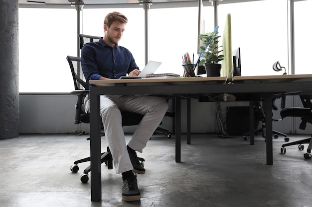 Hombre de negocios moderno joven que trabaja con tableta digital mientras está sentado en la oficina.