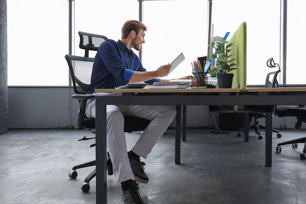 Hombre de negocios moderno joven que trabaja con tableta digital mientras está sentado en la oficina.